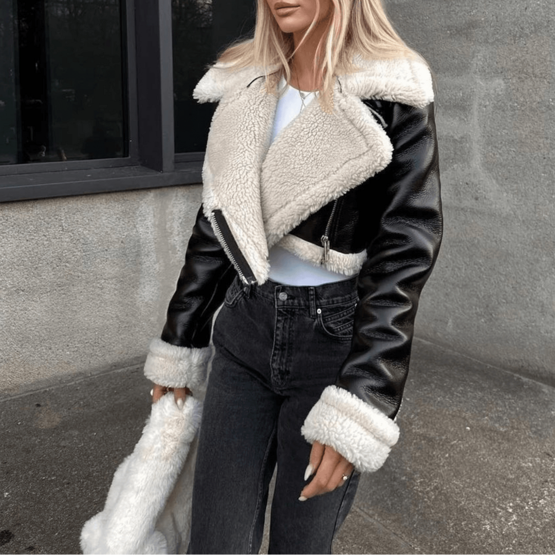 Blonde Frau in schwarzer Lederjacke mit weißem Fellkragen, steht vor modernem Gebäude. Modetrend, Wintermode, stilvolle Damenbekleidung.