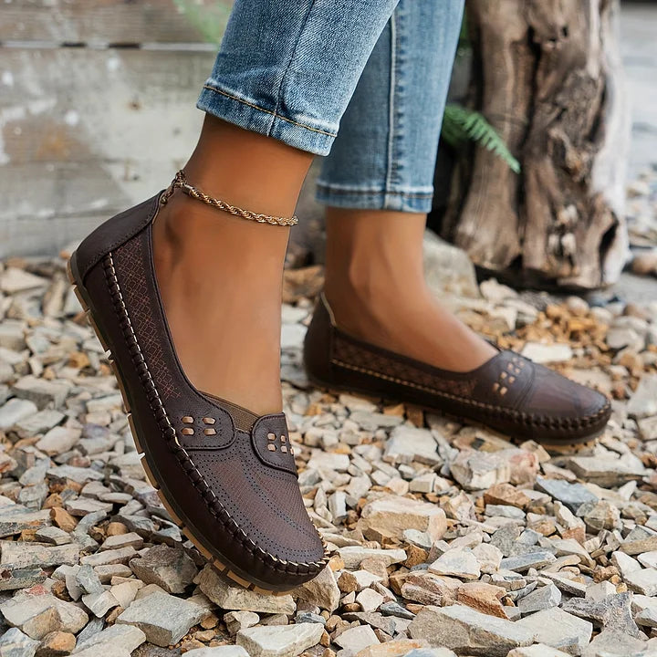 Damen Mokassins in Dunkelbraun auf Kiesweg, kombiniert mit blauen Jeans. Bequeme, stilvolle Schuhe für Freizeit und Alltag.