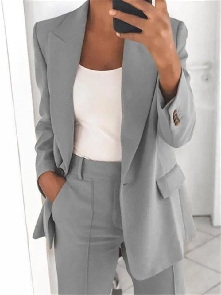 Frau im grauen Anzug mit weißem Top, hält Smartphone, moderne Businessmode, eleganter Look, Büro-Outfit, stilvolle Damenbekleidung.