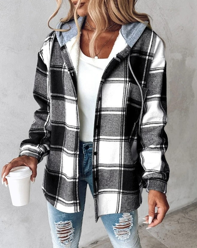 Frau in kariertem Hoodie mit Kaffeebecher, weiße Bluse, zerrissene Jeans. Modetrend Herbst, lässiger Streetstyle, gemütlicher Look.