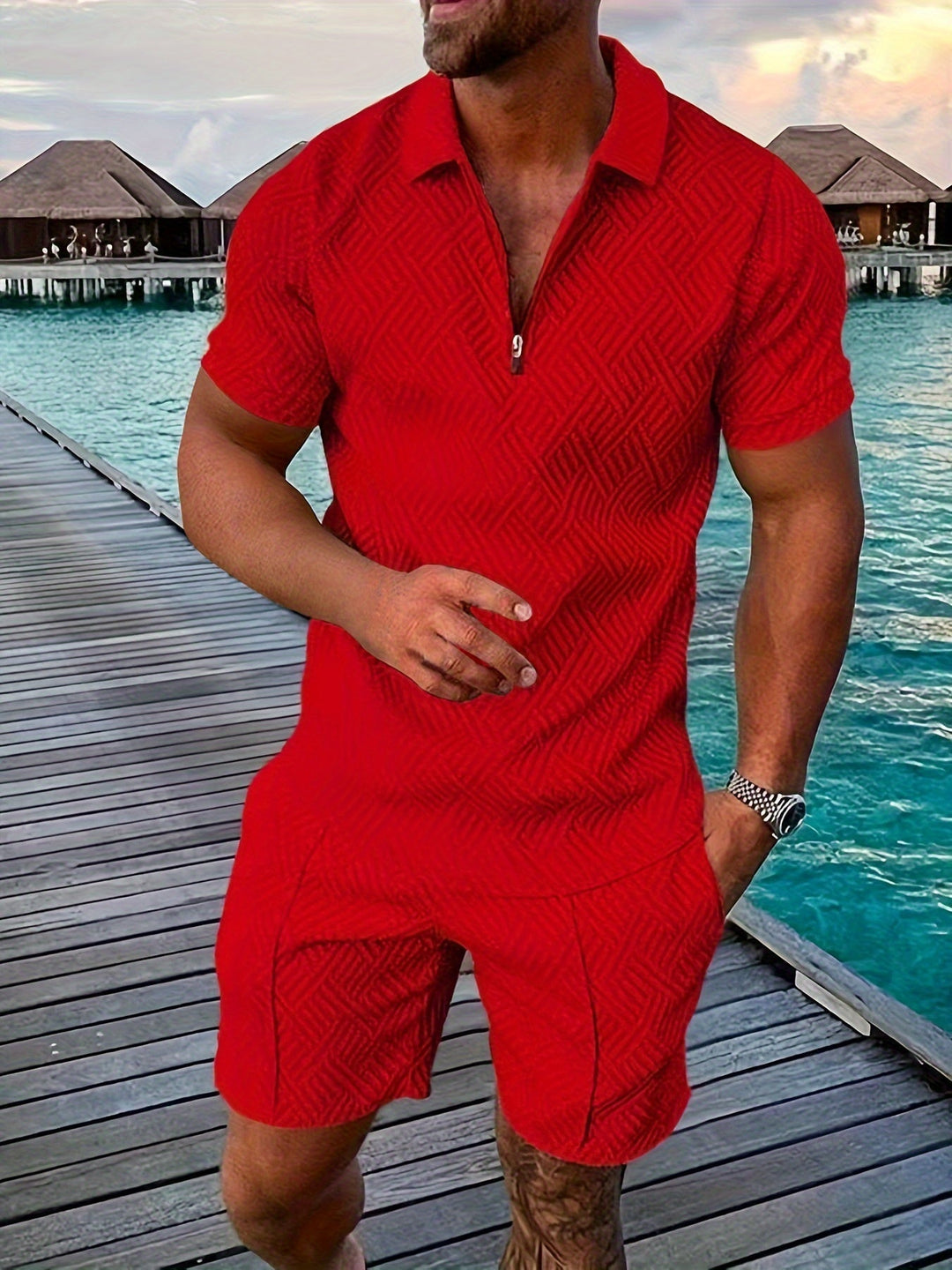 Mann in rotem Sommeroutfit auf Holzsteg am Meer, im Hintergrund Wasserbungalows. Mode, Herrenbekleidung, Urlaub, tropische Kulisse.