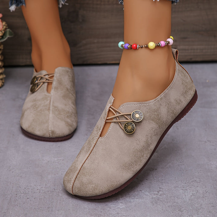 Beige Damen-Loafer mit dekorativen Knöpfen und bunter Perlenkette am Knöchel, modische Freizeitschuhe auf grauem Boden.