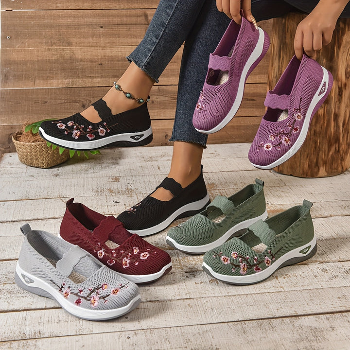 Frau trägt lila bestickte Sneakers, umgeben von vier Paaren in verschiedenen Farben auf Holzboden. Modische, bequeme Damenschuhe mit Blumenmuster.