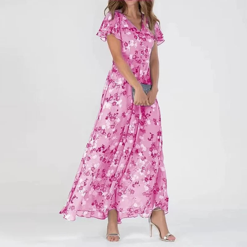 Frau in langem, rosa geblümtem Kleid mit V-Ausschnitt und kurzen Ärmeln, hält eine silberne Clutch, trägt silberne High Heels. Elegante Abendmode.