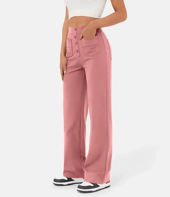 Frau trägt rosa Schlaghose mit Knöpfen und weißem Top, kombiniert mit schwarz-weißen Sneakern. Modetrend, Damenmode, lässiger Stil.