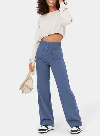 Frau in weißem Crop-Top und blauer Schlaghose mit Knöpfen, hält eine beige Tasche. Modetrend, Freizeitlook, Damenbekleidung.