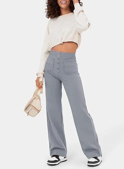 Frau in modischer, weißer Crop-Top-Bluse und blauer High-Waist-Hose mit Knöpfen, hält eine beige Tasche, trägt schwarz-weiße Sneaker.