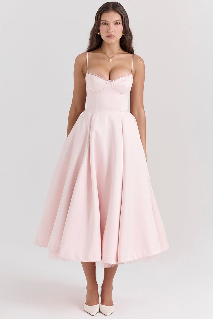 Frau in elegantem, rosa Cocktailkleid mit Spaghettiträgern und ausgestelltem Rock, kombiniert mit weißen Pumps. Perfekt für Abendveranstaltungen.