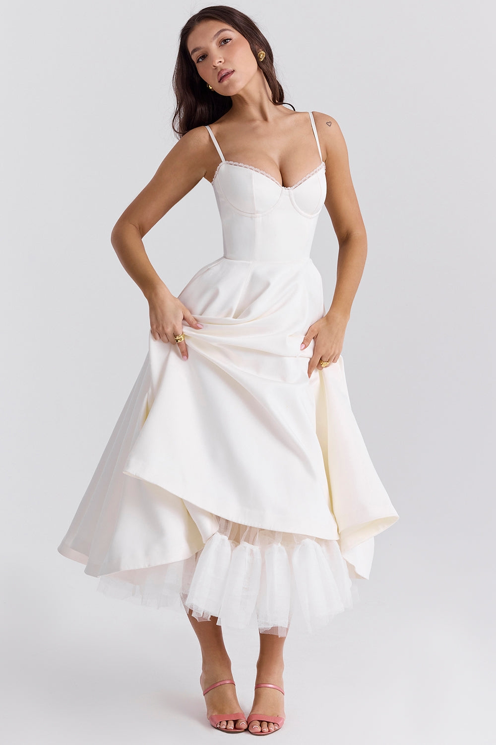 Frau in elegantem weißen Kleid mit Spaghettiträgern und ausgestelltem Rock, posiert vor neutralem Hintergrund. Perfekt für Hochzeits- oder Abendmode.