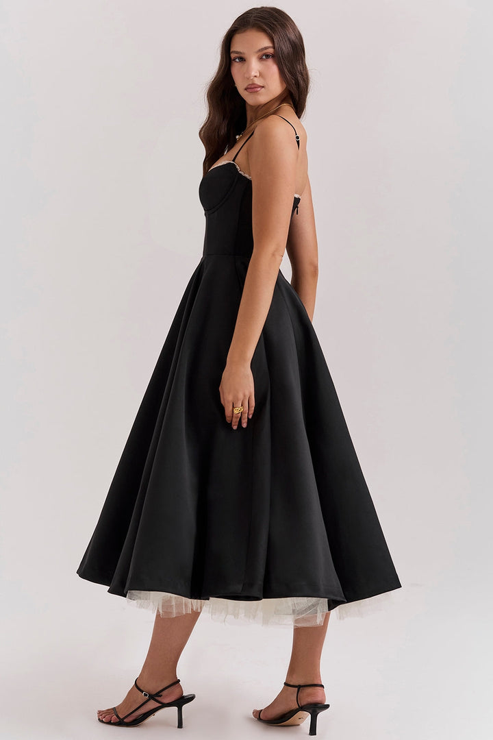 Frau in elegantem, schwarzem Abendkleid mit Spaghettiträgern und ausgestelltem Rock, trägt schwarze Sandaletten. Perfekt für formelle Anlässe.