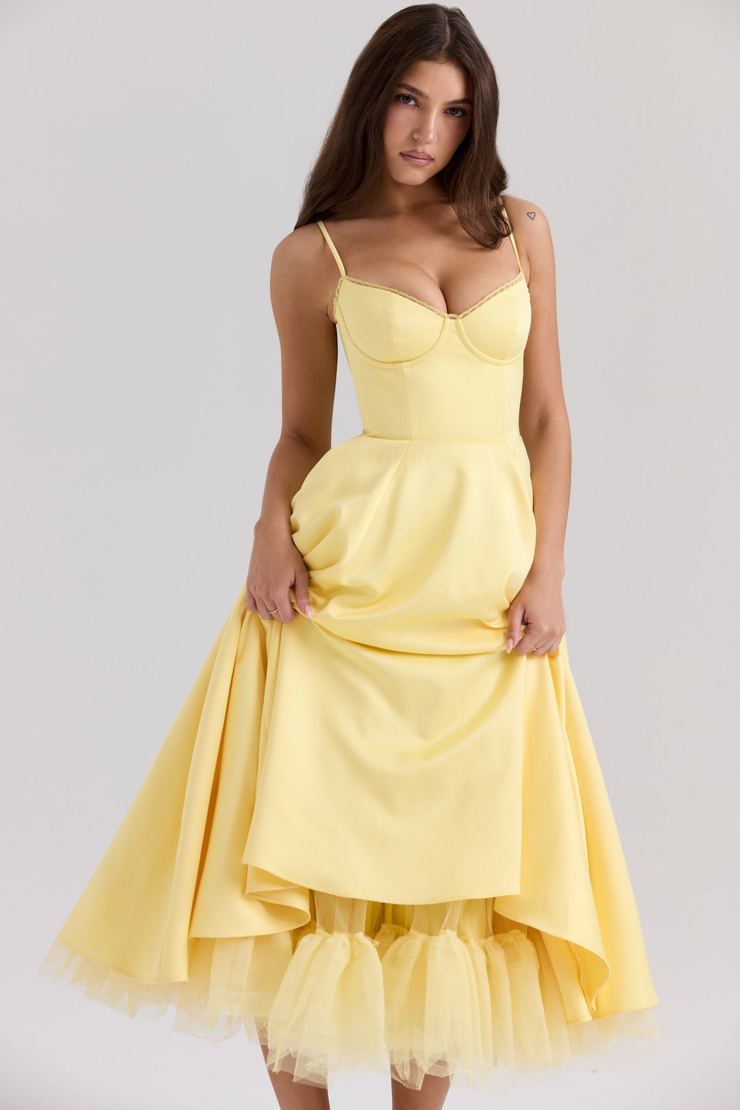 Frau in elegantem gelbem Kleid mit Spaghettiträgern und voluminösem Rock, posiert vor neutralem Hintergrund. Fashion, Abendmode, Damenkleidung.
