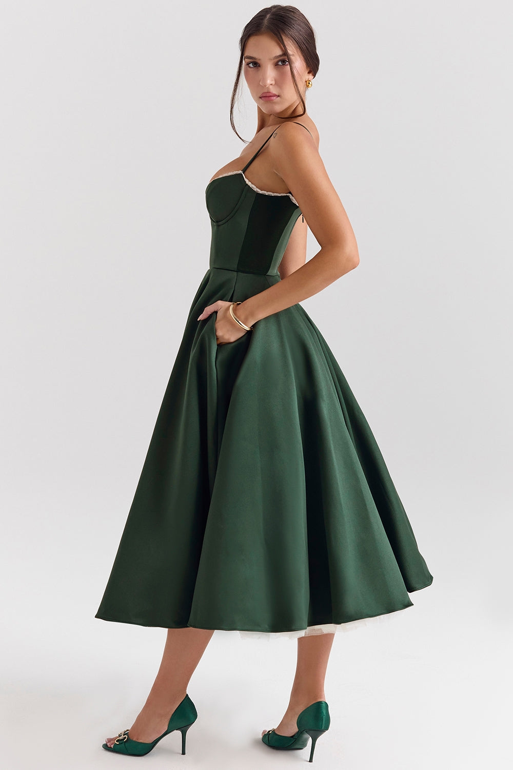 Frau in elegantem, grünem Abendkleid mit Spaghettiträgern und weitem Rock, kombiniert mit passenden grünen High Heels, vor weißem Hintergrund.