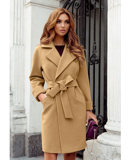 Frau in elegantem, beigem Trenchcoat mit Gürtel, steht vor einem schmiedeeisernen Tor. Herbstmode, stilvoller Mantel, Damenbekleidung.