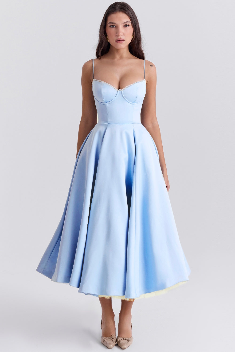 Frau in elegantem, hellblauem Abendkleid mit Spaghettiträgern und ausgestelltem Rock, stehend vor neutralem Hintergrund.
