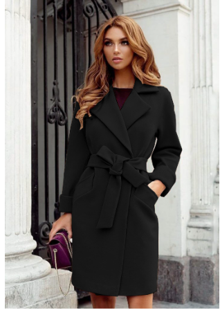 Frau in elegantem schwarzen Mantel mit Gürtel, steht vor klassischer Architektur. Mode, Herbst, Damenbekleidung, stilvoll, urban.