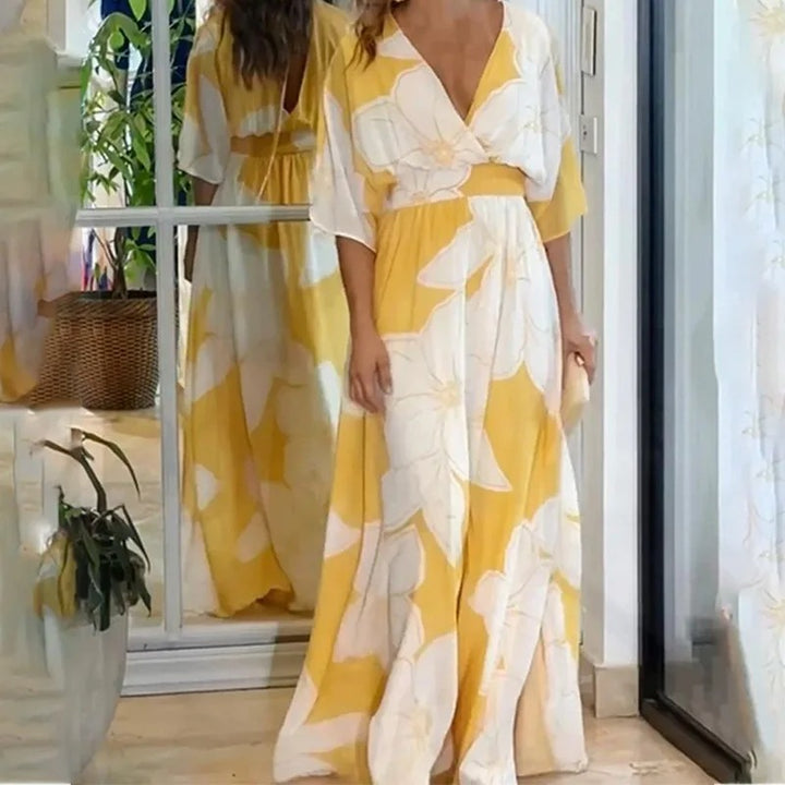 Frau in gelbem Maxikleid mit weißen Blumen, steht vor einem Spiegel. Sommermode, elegantes Blumenkleid, Freizeitkleidung, Innenraum.