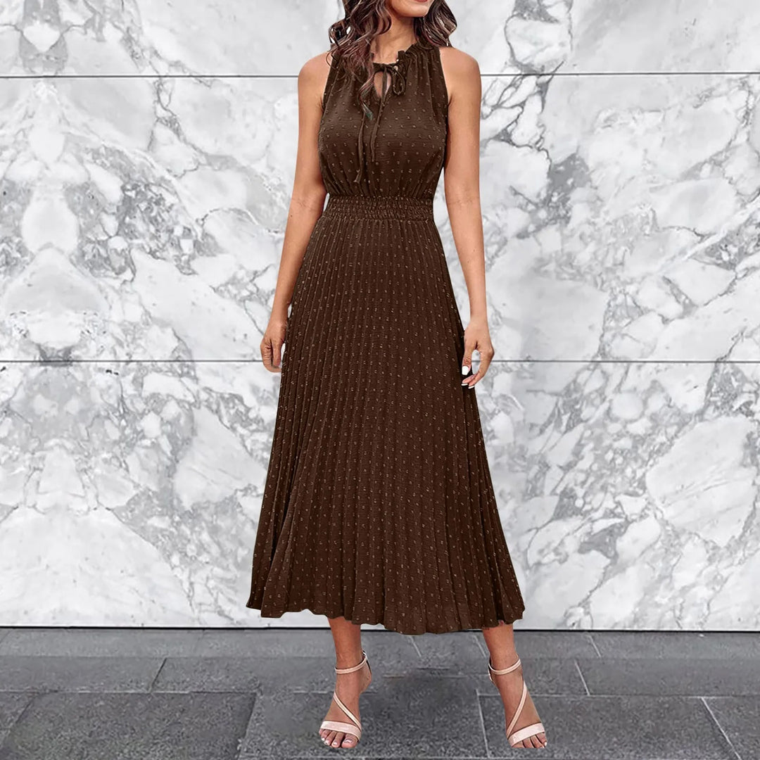 Braunes, ärmelloses Kleid mit Plissee-Design vor marmorierter Wand. Elegantes Damenoutfit, ideal für Sommermode und festliche Anlässe.