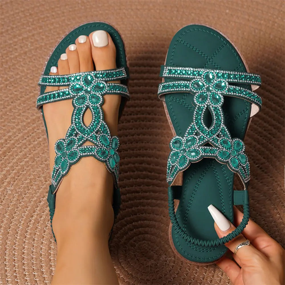 Grüne Sandalen mit Strasssteinen, Blumenmuster und verstellbaren Riemen auf geflochtenem Teppich. Elegante Sommerschuhe für Damen.