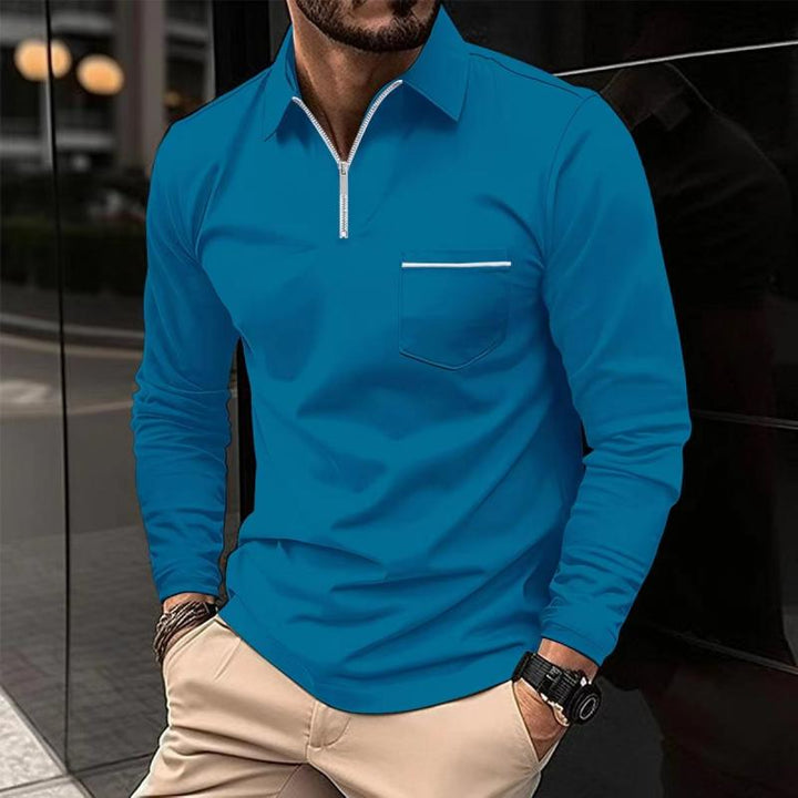 Mann in blauem Langarm-Poloshirt mit Reißverschluss und Brusttasche, beige Hose, Armbanduhr, städtischer Hintergrund. Herrenmode, Freizeitlook.