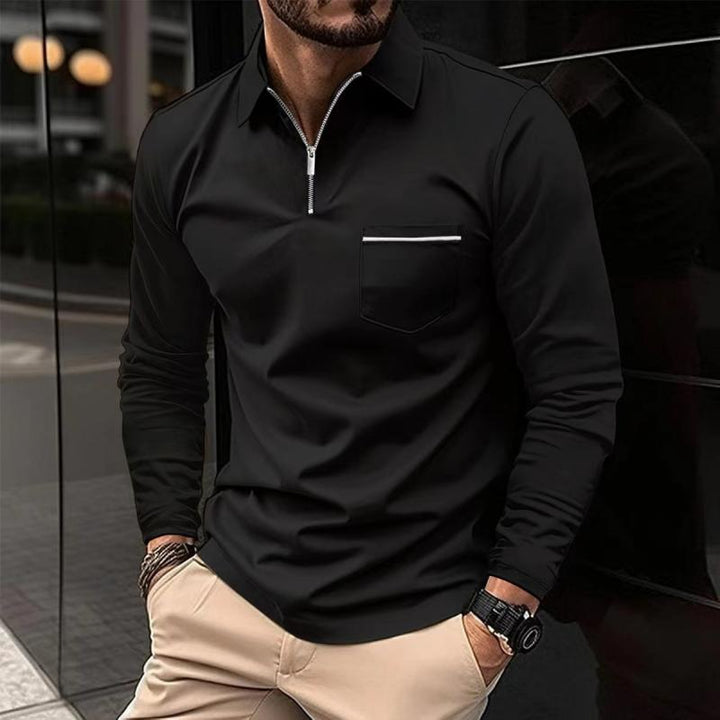 Mann in schwarzem Langarm-Poloshirt mit Reißverschluss und beiger Hose, steht vor einem modernen Gebäude. Elegante Herrenmode, urbaner Stil.