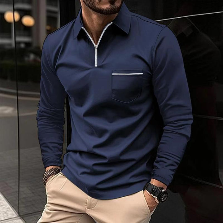 Mann in dunkelblauem Langarmshirt mit Reißverschluss und Brusttasche, kombiniert mit beigen Hosen. Elegante Herrenmode, urbaner Stil.