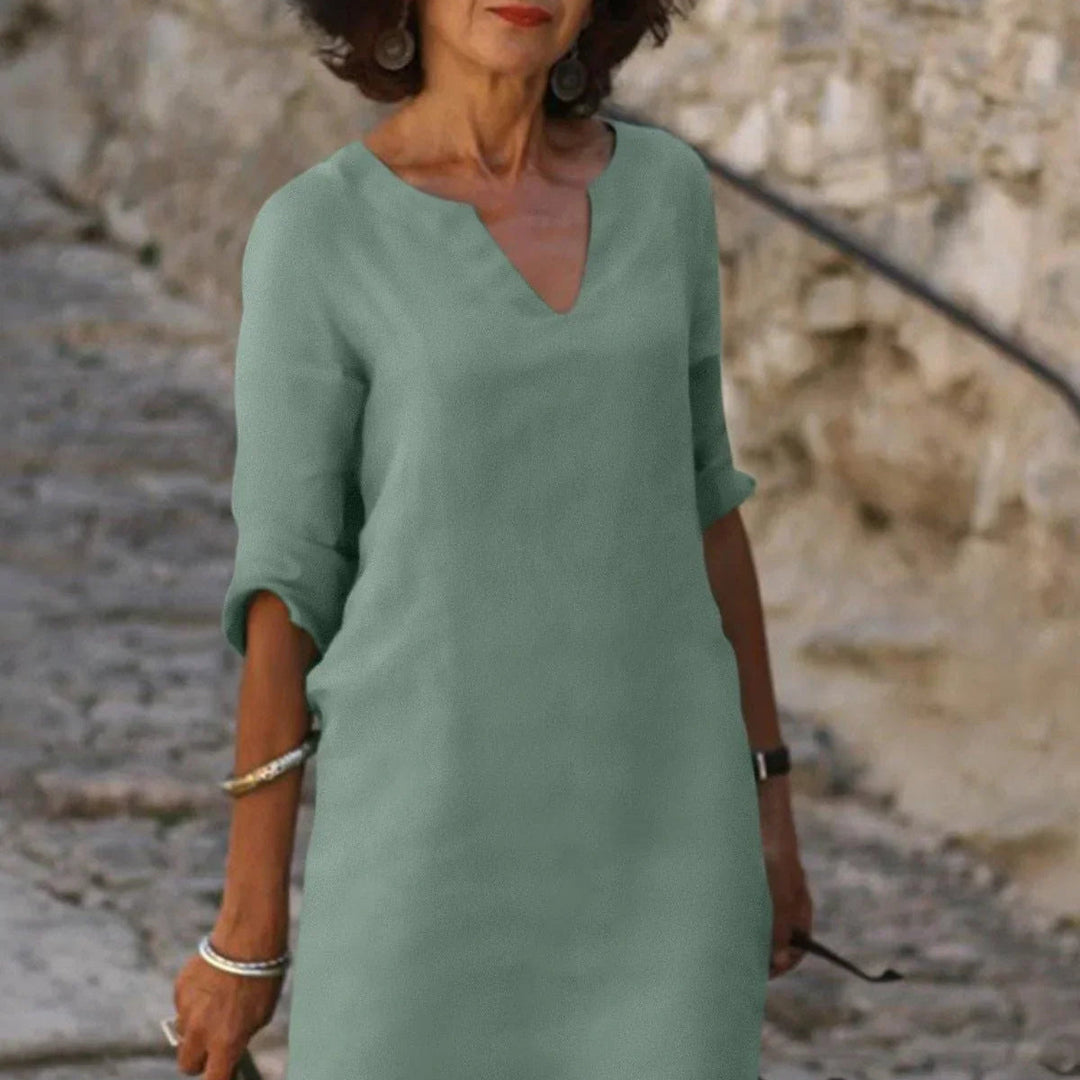 Eine Frau in einem eleganten, grünen Kleid mit V-Ausschnitt steht auf einer steinigen Treppe. Sie trägt Armreifen und Ohrringe.