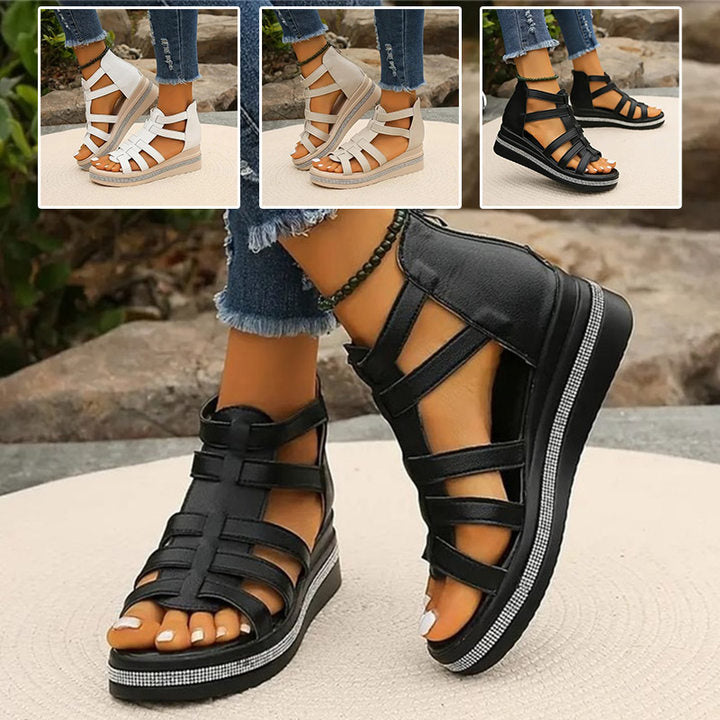 Schwarze Sandalen mit Keilabsatz und Riemen, getragen von einer Person auf Steinboden. Drei weitere Farbvarianten im Hintergrund. Modische Sommerschuhe.
