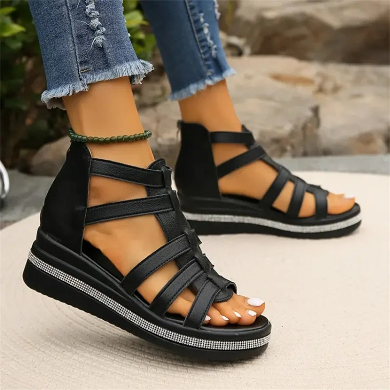 Schwarze Damen-Sandalen mit Keilabsatz, Riemchen-Design und Strassdetails, getragen mit zerrissenen Jeans. Ideal für Sommermode und Freizeitoutfits.