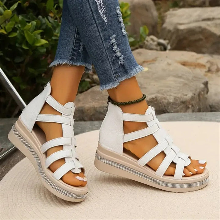 Damenfüße in weißen Sandalen mit Keilabsatz, kombiniert mit zerrissenen Jeans, auf Steinweg. Modische Sommerschuhe, bequeme Sandalen.