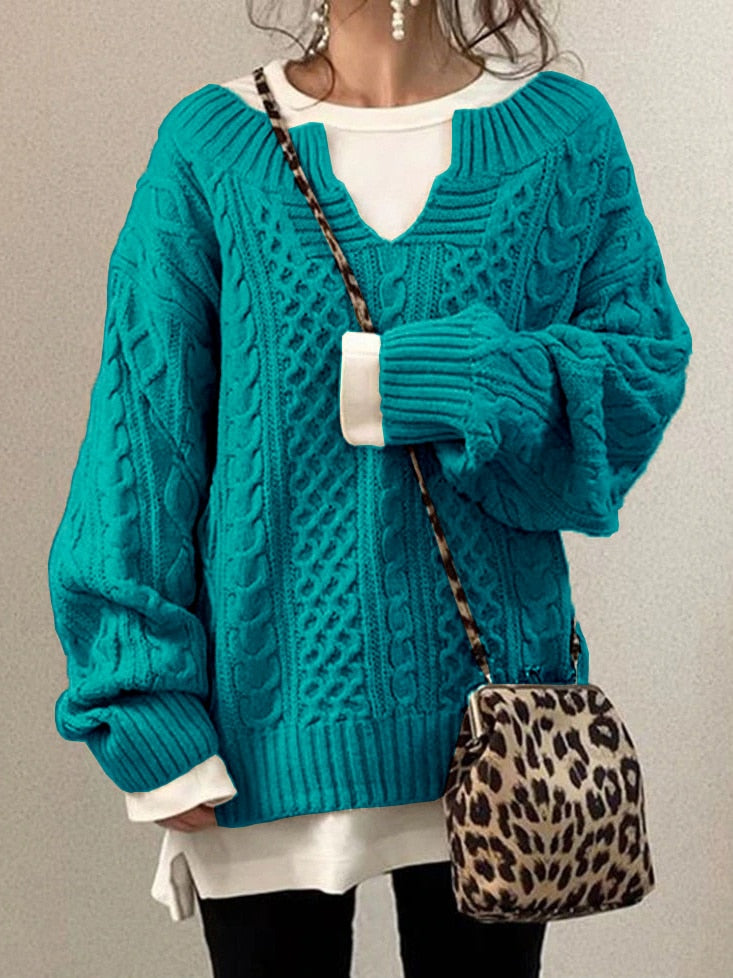 Frau in türkisfarbenem Strickpullover mit Zopfmuster, weißem Shirt darunter, hält eine Leopardenmuster-Tasche. Modetrend, Herbstmode, Strickmode.