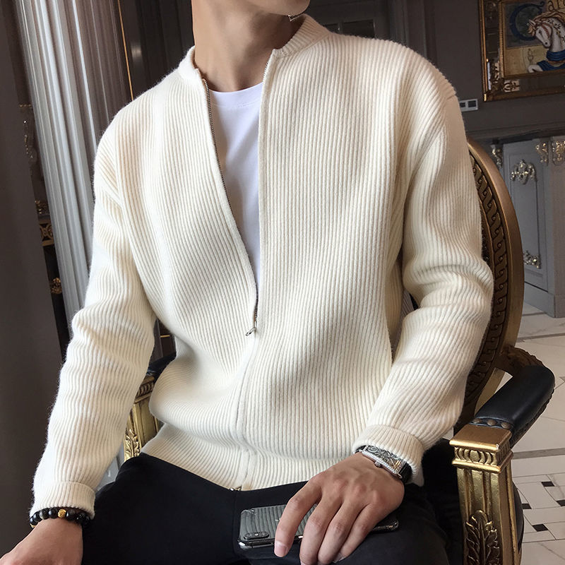 Mann in weißer Strickjacke mit Reißverschluss, sitzt auf einem Stuhl, hält ein Smartphone. Elegante Herrenmode, stilvoller Freizeitlook.