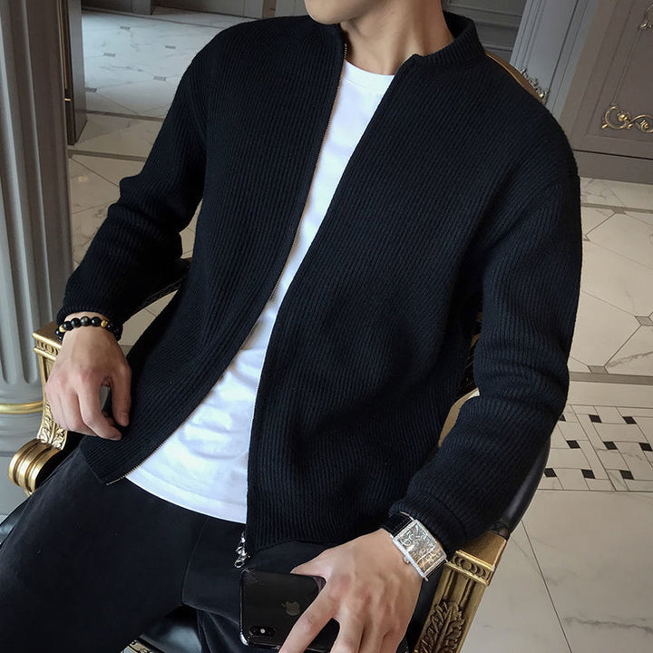 Mann in schwarzer Strickjacke und weißem T-Shirt sitzt auf Stuhl, hält Smartphone, trägt Armbanduhr. Elegante Herrenmode, Freizeitlook.