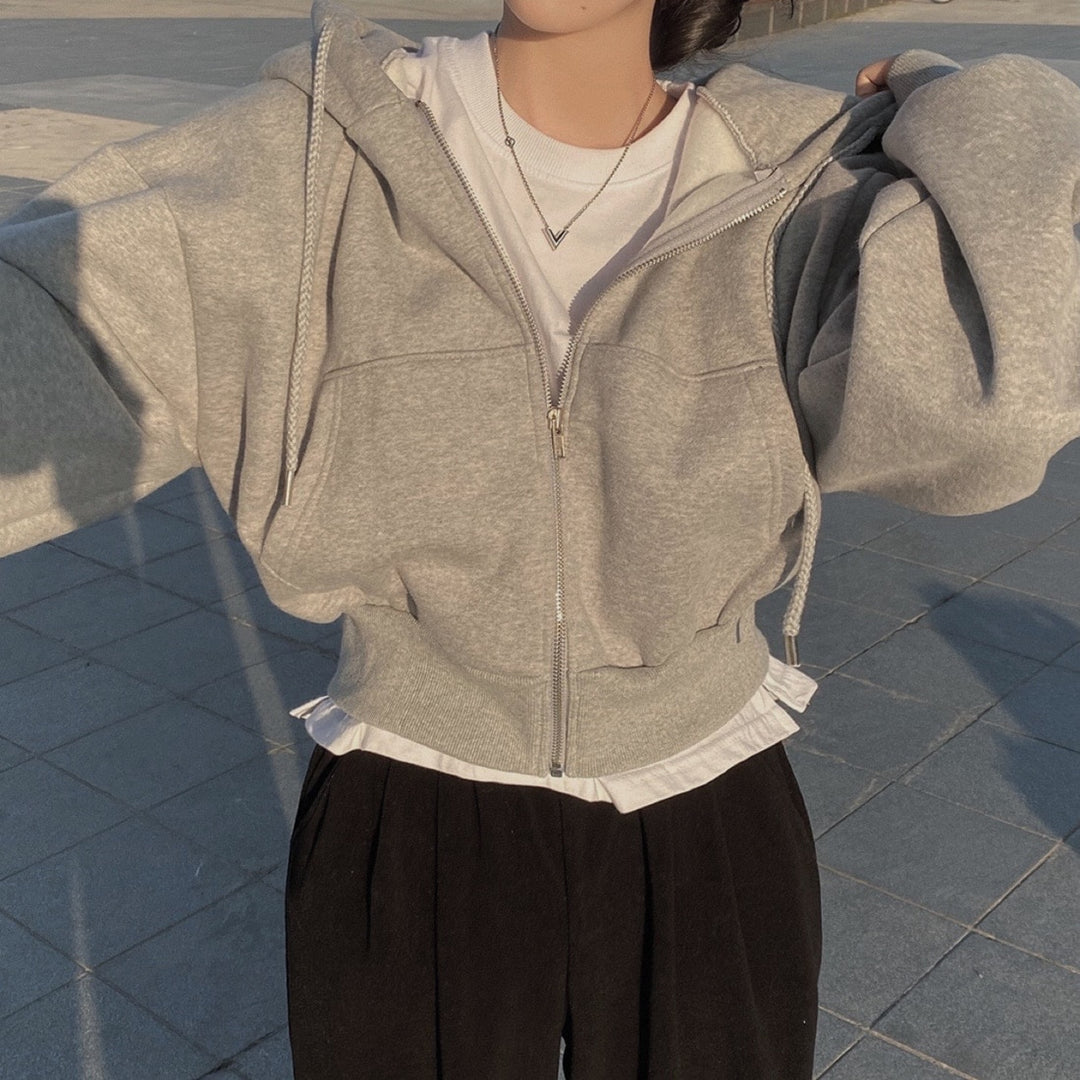 Frau in grauem Hoodie und weißem T-Shirt, trägt schwarze Hose. Modetrend, lässiger Stil, Herbstmode, urbaner Look, Streetwear.