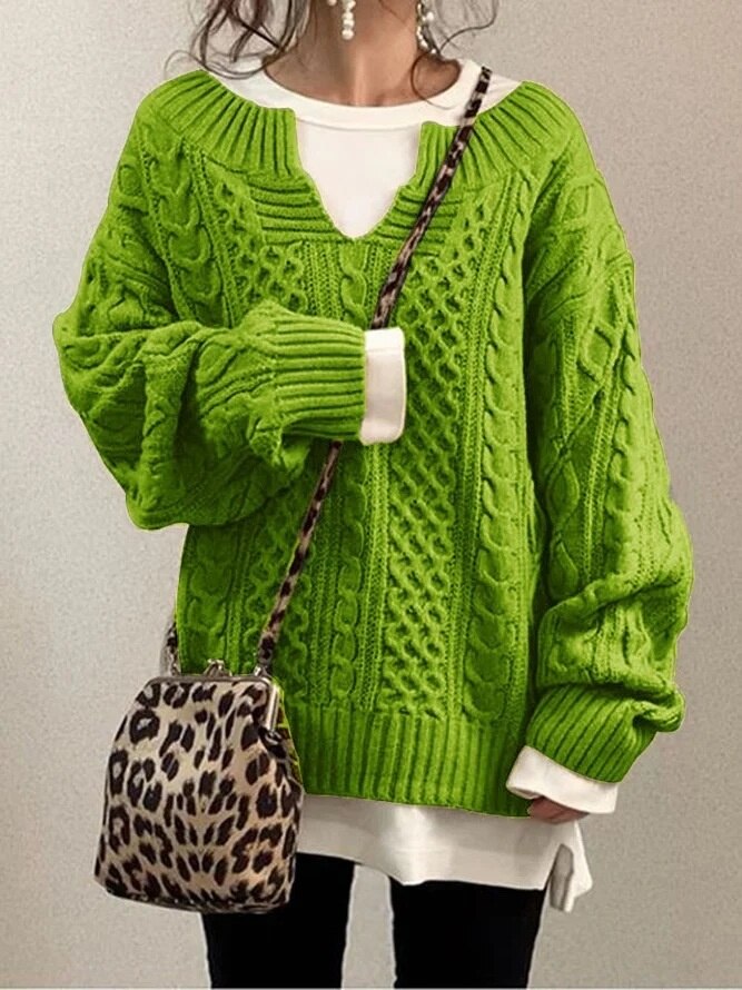Frau in grünem Strickpullover mit Zopfmuster, weißem Shirt darunter, hält eine Leopardenmuster-Tasche. Modetrend, Herbstmode, Strickmode.