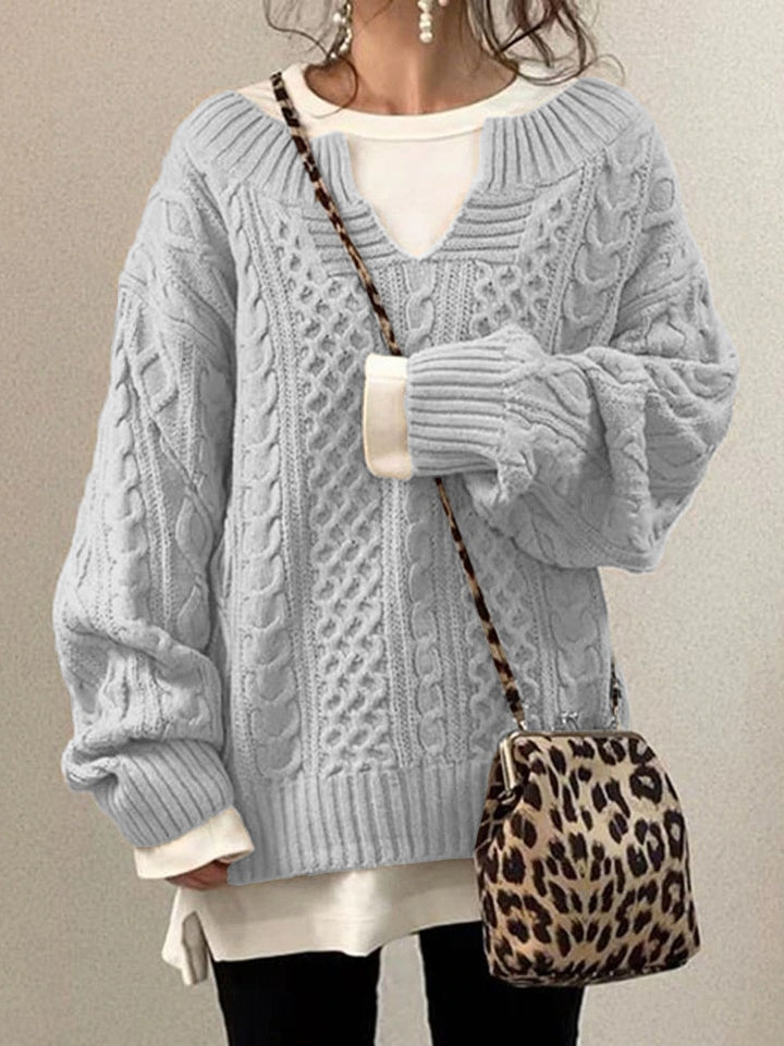 Frau in grauem Strickpullover mit Zopfmuster, trägt eine Leopardenmuster-Tasche. Modetrend, Herbstmode, gemütlicher Look.