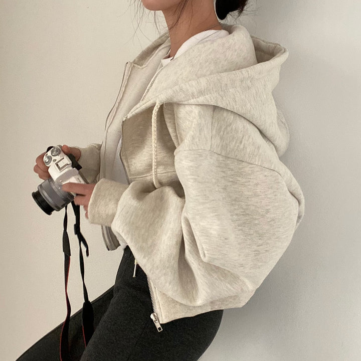 Frau in grauem Hoodie hält Kamera, modischer Freizeitlook, Fotografie-Enthusiast, stilvolle Damenbekleidung, moderne Streetwear.