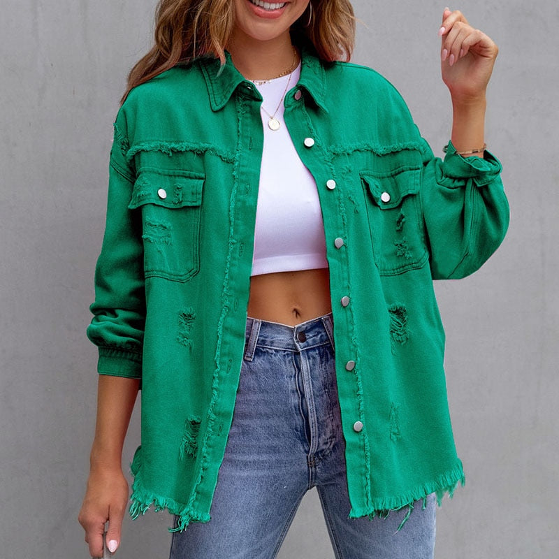 Frau in grüner, zerrissener Jeansjacke, weißem Crop-Top und blauen Jeans vor grauem Hintergrund. Modetrend, lässiger Stil, Streetwear.