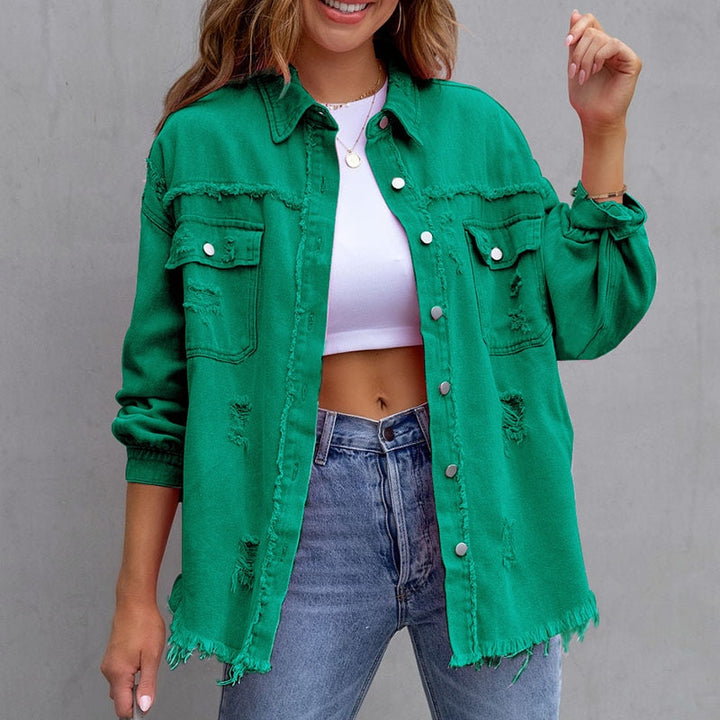 Frau in grüner, zerrissener Jeansjacke, weißem Crop-Top und blauen Jeans vor grauem Hintergrund. Modetrend, lässiger Stil, Streetwear.