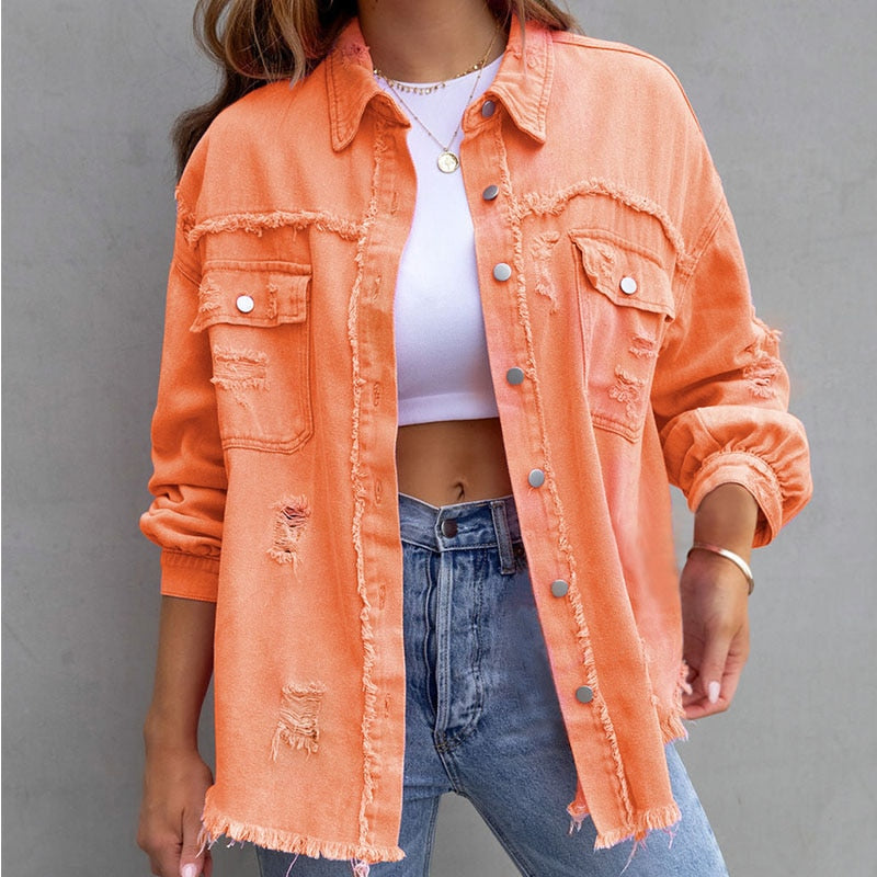 Frau in zerrissener orangefarbener Jeansjacke, weißem Top und blauen Jeans vor grauem Hintergrund. Modetrend, lässiger Stil, Damenmode.