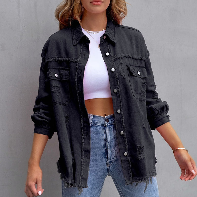 Frau in schwarzer Jeansjacke, weißem Crop-Top und blauen Jeans vor grauem Hintergrund. Modetrend, lässiger Stil, Damenbekleidung.