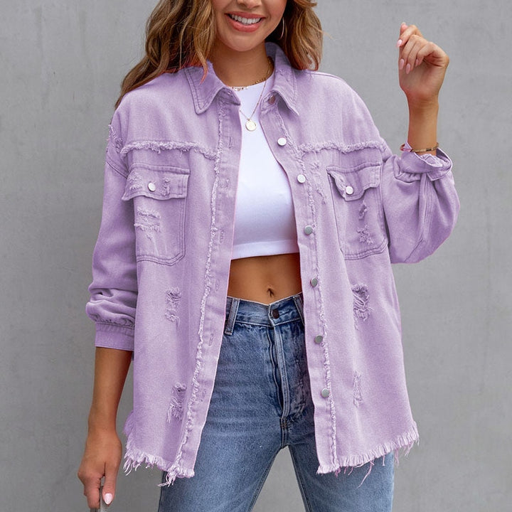 Frau trägt lila Jeansjacke, weißes Top und Jeans. Modetrend, lässiger Streetstyle, Damenmode, Fransenjacke, urbaner Look.