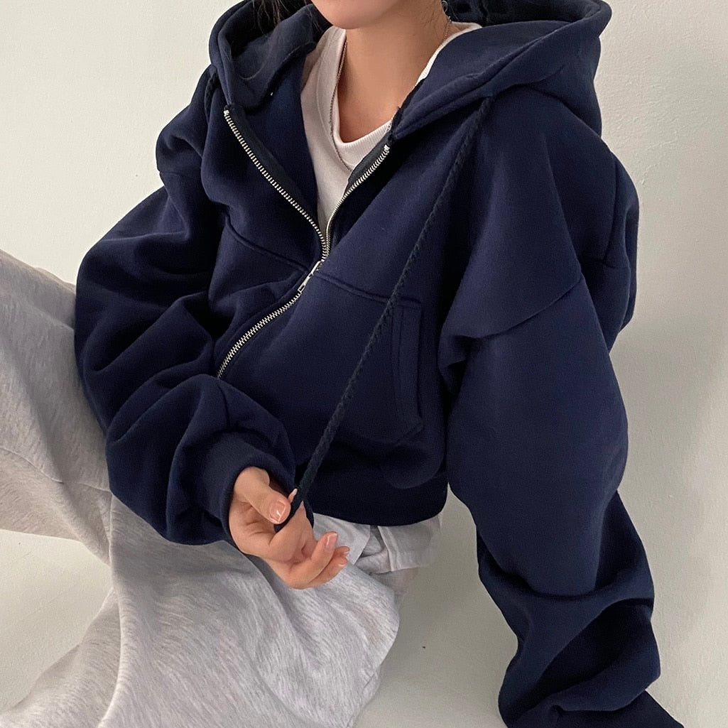 Frau in dunkelblauem Hoodie und grauer Jogginghose sitzt entspannt. Bequeme Freizeitmode, lässiger Stil, gemütlicher Look.