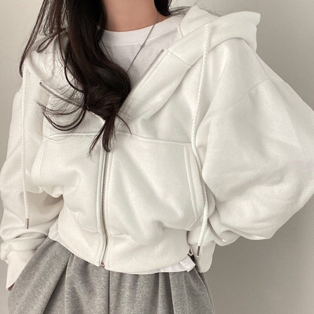 Weiße Kapuzenjacke mit Reißverschluss, getragen von Frau mit langen Haaren. Modetrend, lässiger Stil, bequeme Freizeitkleidung.