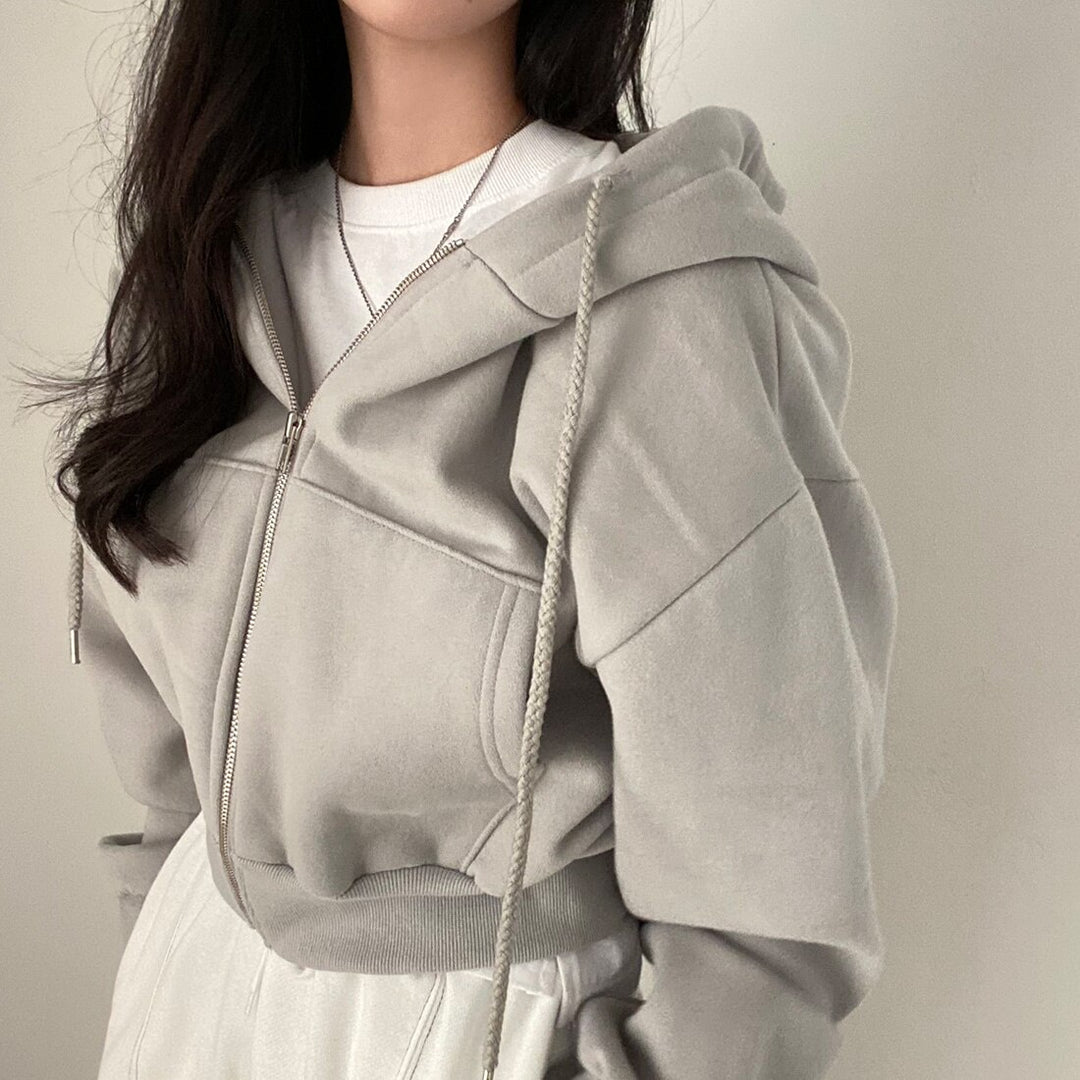Frau in grauem Kapuzenpullover mit Reißverschluss, lässiger Stil, modische Freizeitkleidung, minimalistisch, trendige Damenmode.