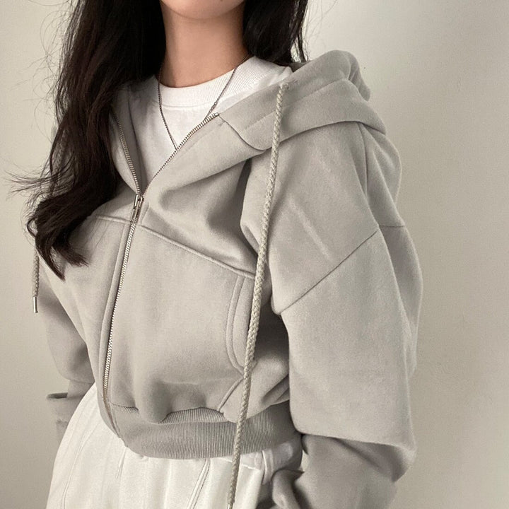 Frau in grauem Kapuzenpullover mit Reißverschluss, lässiger Stil, modische Freizeitkleidung, minimalistisch, trendige Damenmode.