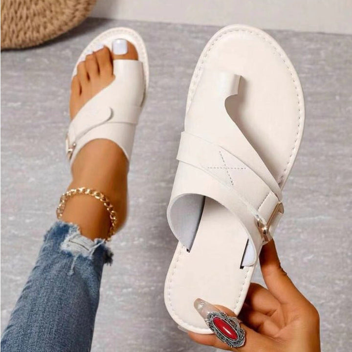 Weiße Damen-Sandalen mit Zehenschlaufe, getragen von einer Person mit Jeans und Fußkettchen. Modische Sommerschuhe, ideal für Freizeitoutfits.