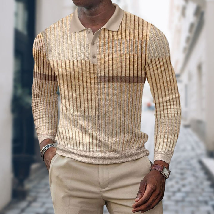 Mann in beigem, gestreiftem Strickpullover und beiger Hose auf gepflasterter Straße. Elegante Herrenmode, Herbstoutfit, urbane Kulisse.
