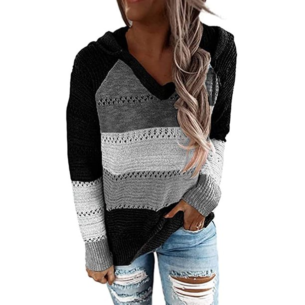 Frau trägt gestreiften Pullover in Schwarz, Grau und Weiß mit Kapuze, kombiniert mit zerrissenen Jeans. Modischer Herbst-Look, lässiger Stil.