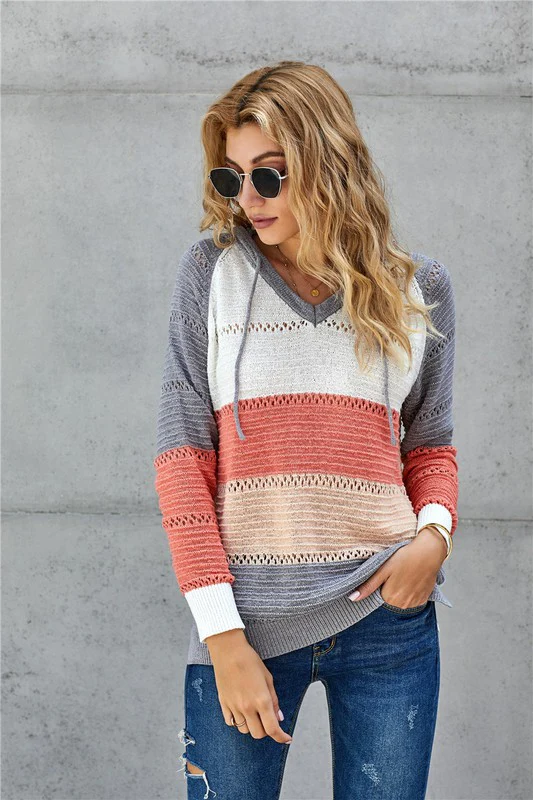 Blonde Frau mit Sonnenbrille trägt gestreiften Strickpullover in Grau, Weiß und Koralle, kombiniert mit zerrissenen Jeans vor grauer Wand.
