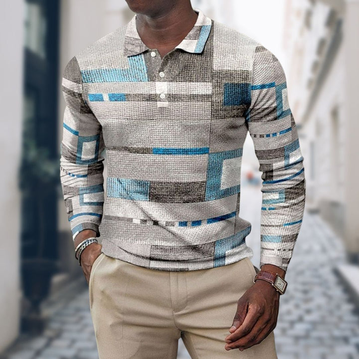 Mann trägt stilvolles, geometrisch gemustertes Langarmhemd in Blau und Grau, kombiniert mit beigen Hosen. Mode, Herrenbekleidung, urbaner Stil.